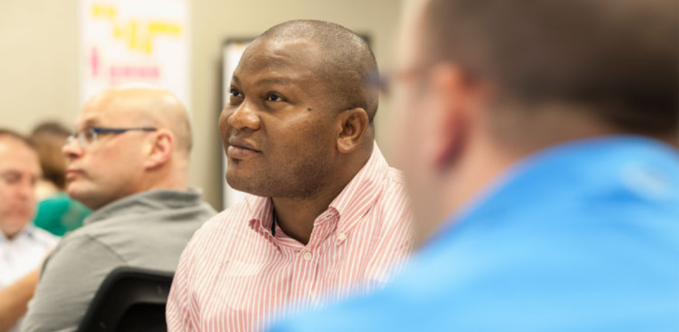 Male learner in classroom looking at front of room surrounded by blurred classmates