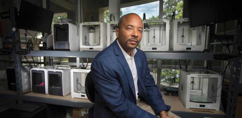 Raheem Beyah looking at camera thoughtfully as he sits in an additive manufacturing lab at Georgia Tech