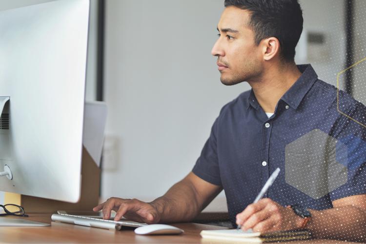 Male employee in front of a computer, taking notes and engaging with content on screen.