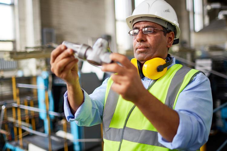 Employee in manufacturing setting in hard hat and safety gear inspecting a piece of equipment