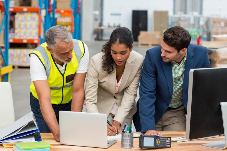 Three logistics professionals collaborating over computer in warehouse