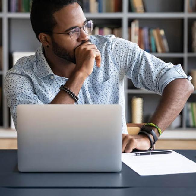 Male professional working on laptop while looking to the side in thought