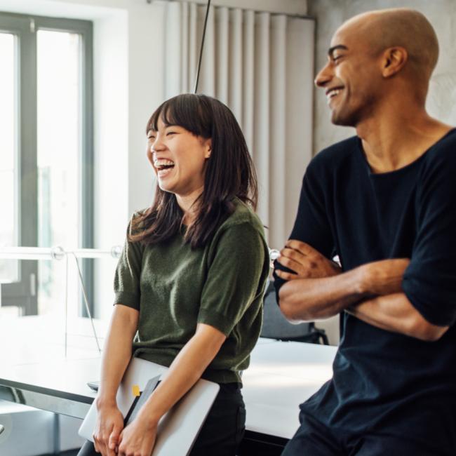 A group of colleagues gathered in a conference room or work area talking and smiling. 