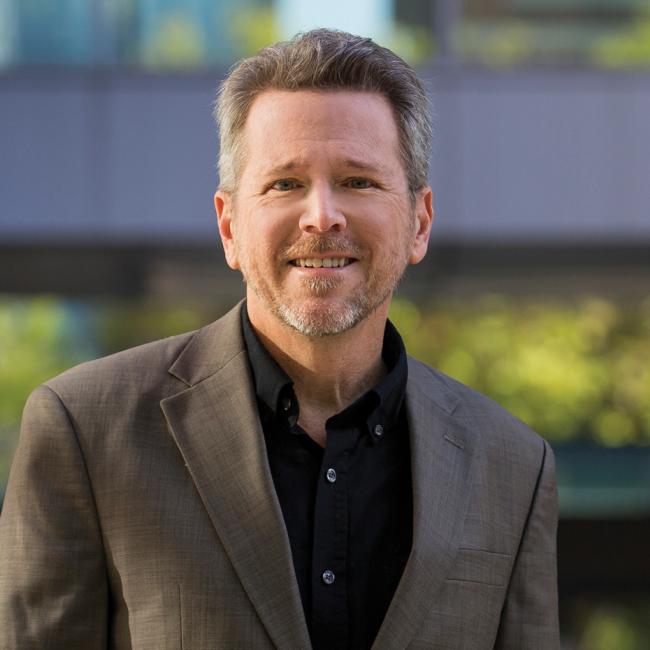 Glenn Hopkins smiling at camera. The background behind him is blurred.